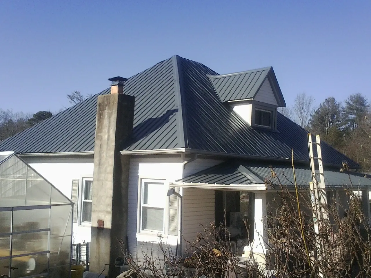 Dark blue standing seam metal roof on a white farmhouse with dormer — Slate & Tile Roof Repair by Roofing Brothers in Sag Harbor