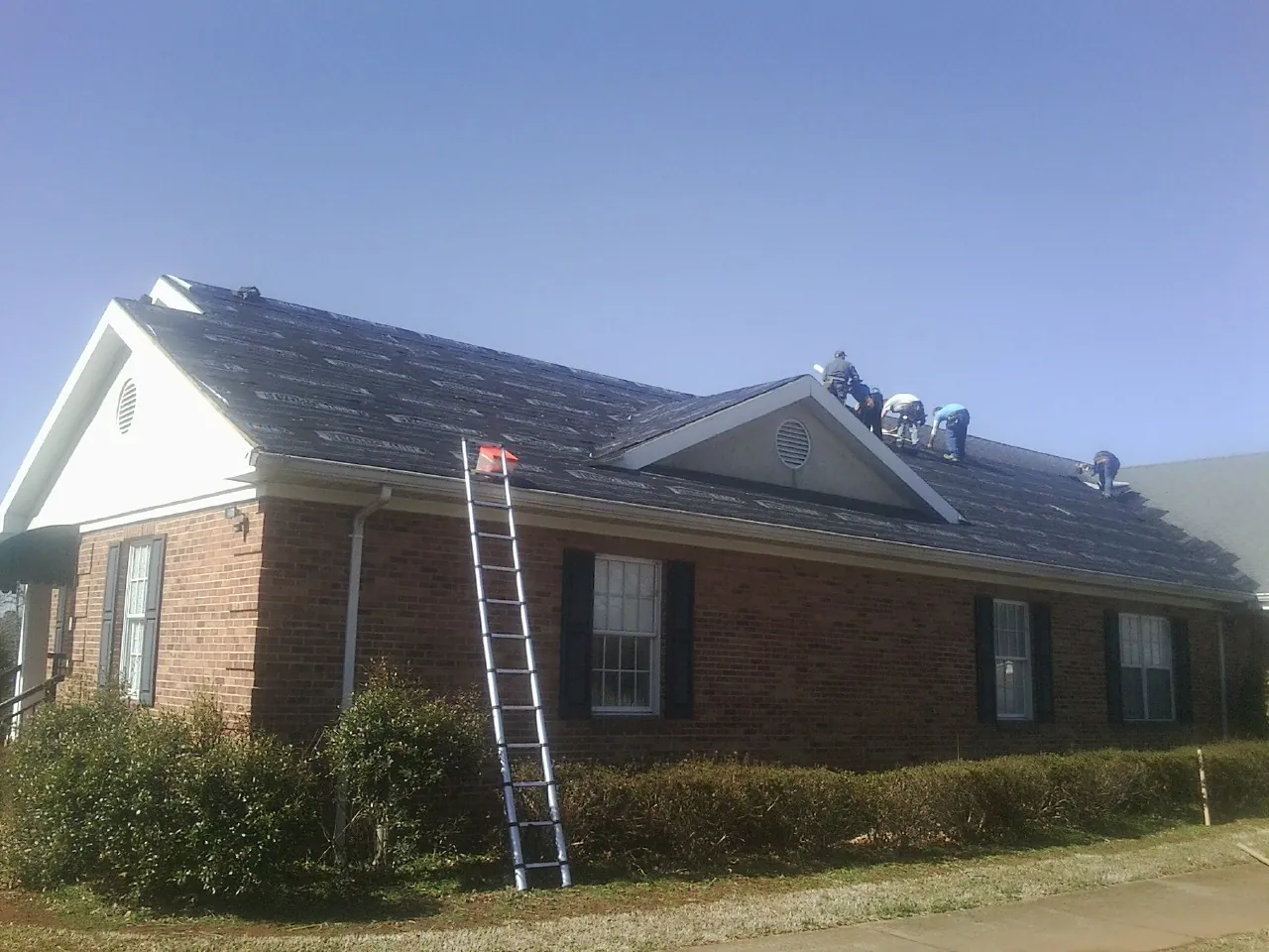 Crew tearing shingles off a brick ranch roof with a ladder set — Emergency Roof Repair work by our crew in Sag Harbor