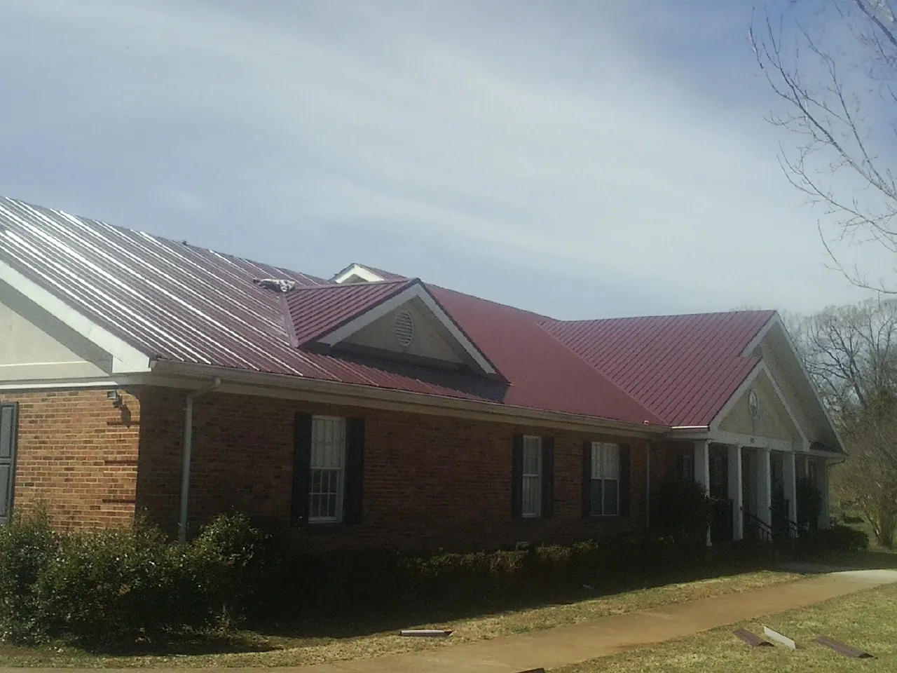 Red metal roof with gabled entries on a long brick building, from a Hail Damage Roof Repair job in Sag Harbor