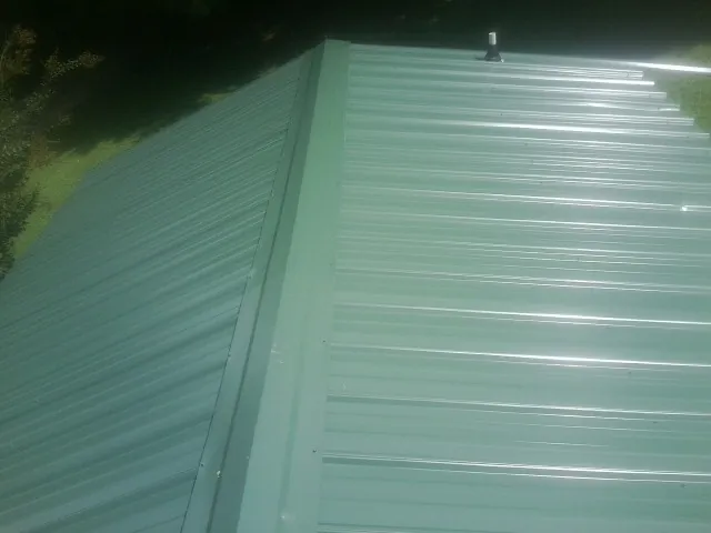 New green metal panels meeting at the ridge of a roof — Flat Roof Repair work by our crew in Sag Harbor