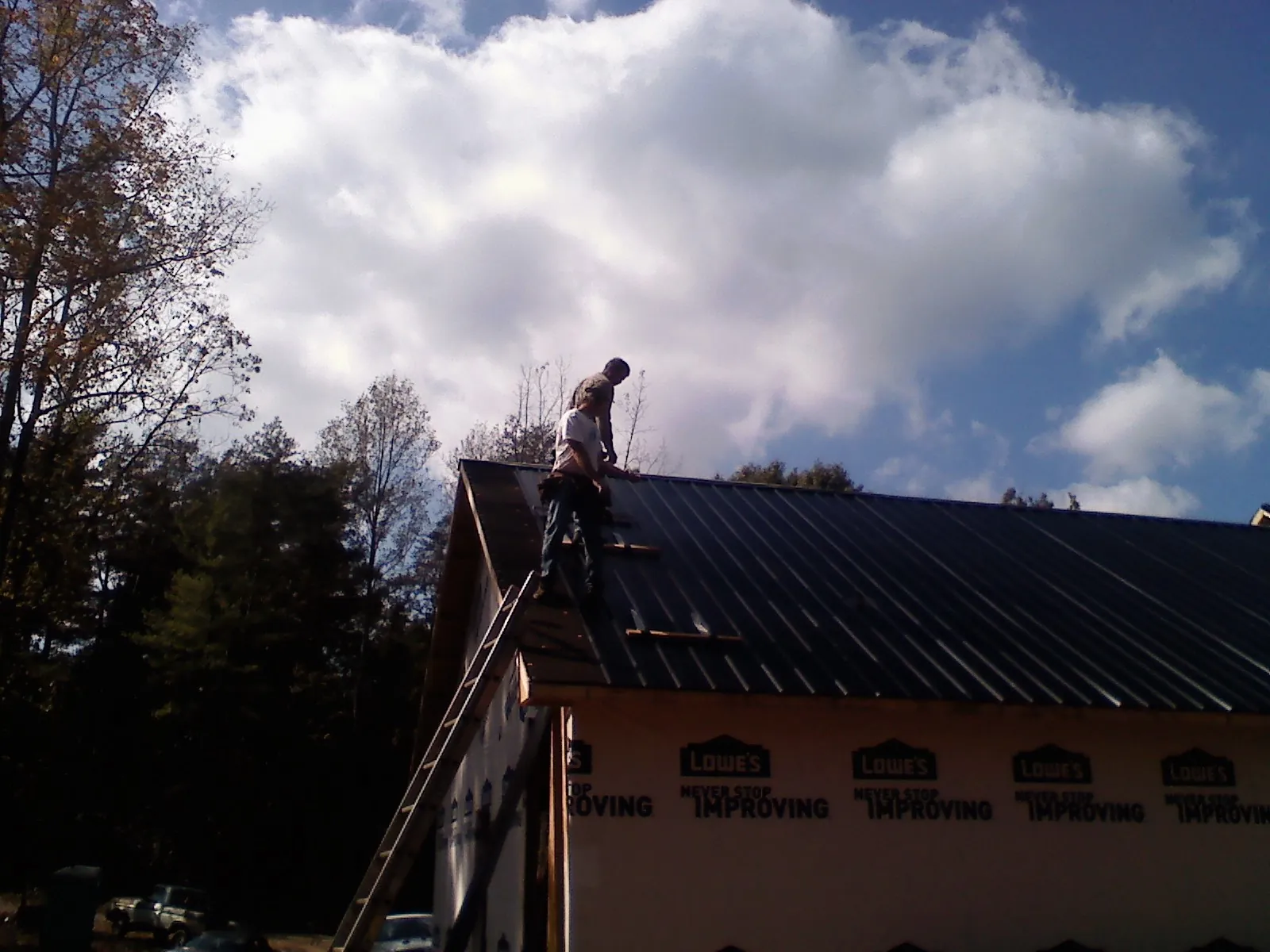 Roofer fastening dark metal panels high against a cloudy sky, from a Roof Inspection job in Sag Harbor