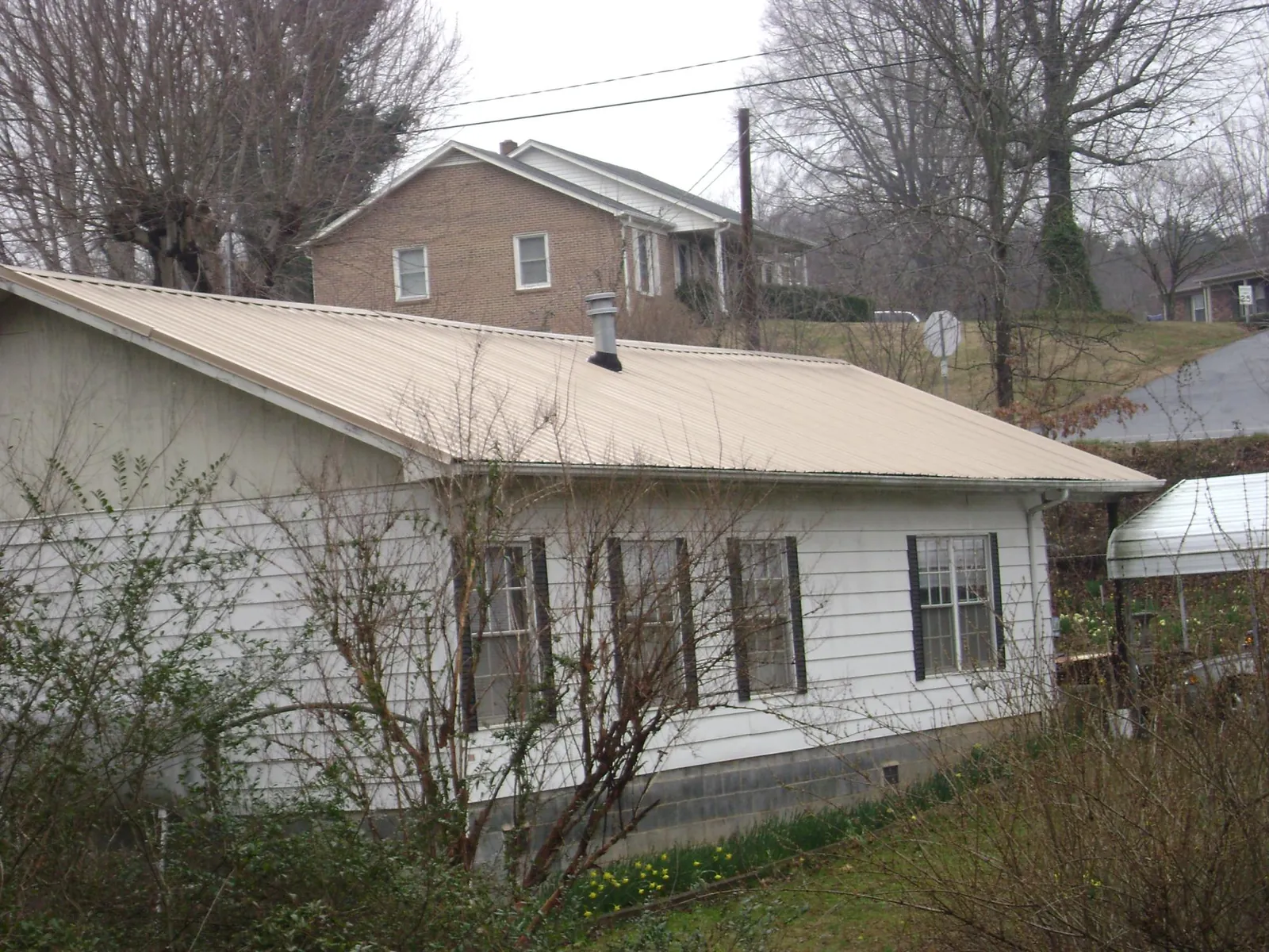 Tan metal roof on a white sided house set into a hillside — Commercial Roofing by Roofing Brothers in Sag Harbor